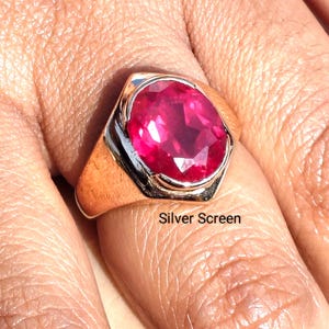 Op de afbeelding: Een ring met een grote, ovaal geslepen, levendige rozerode edelsteen in een gepolijste, goudkleurige metalen band. De zetting heeft een glad, taps toelopend ontwerp dat breder wordt naar het midden, waar de gefacetteerde steen stevig vastzit.