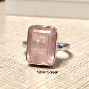 Op de afbeelding: Een zilveren ring met een grote, rechthoekige, gefacetteerde rozenkwarts edelsteen in een gepolijste metalen zetting. De steen heeft een zachte, doorschijnende roze tint met zichtbare insluitingen. De tekst Silver Screen staat eronder gedrukt.