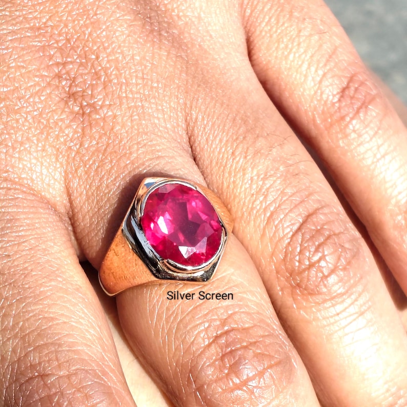 Op de afbeelding: Een ring met een grote, ovaal geslepen, levendige rozerode edelsteen in een gepolijste, goudkleurige metalen band. De zetting heeft een glad, taps toelopend ontwerp dat breder wordt naar het midden, waar de gefacetteerde steen stevig vastzit.