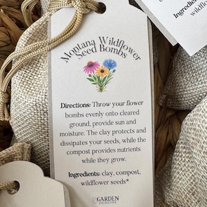 May include: A beige paper tag attached to a burlap drawstring bag with gold cord. The tag features the text Montana Wildflower Seed Bombs, a floral illustration, directions for use, and a list of ingredients including clay, compost, and seeds.