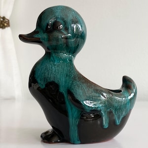 Peut inclure: Une figurine de canard en céramique présentant une glaçure de base noire brillante avec un effet de glaçure goutte à goutte bleu sarcelle vibrant qui coule de la tête et du dos. Le canard a une surface lisse et réfléchissante, une tête arrondie.