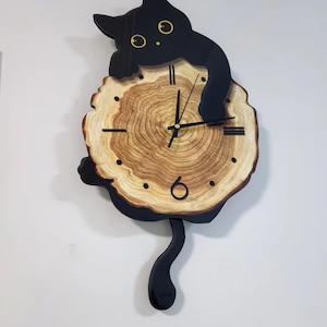 Peut inclure: Une horloge murale fantaisiste avec un chat noir perché sur une tranche de bois. Le cadran de l'horloge présente un motif de grain de bois naturel avec des aiguilles et des marqueurs noirs. Le chat a des yeux jaunes et une queue incurvée.