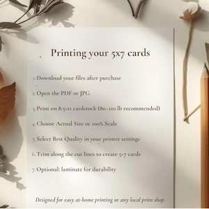 May include: A white sheet of paper with instructions for printing 5x7 cards. The text includes steps for downloading files, opening PDFs, printing on 8.5x11 cardstock, and trimming. The paper is surrounded by dried leaves and a pencil.