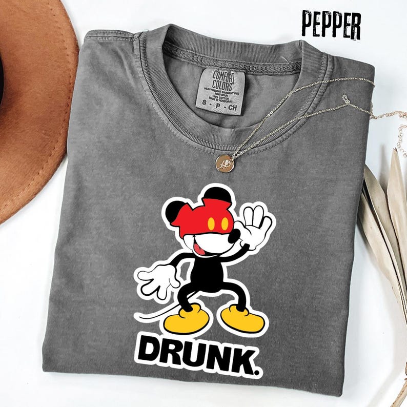 May include: A gray Comfort Colors t-shirt with a graphic of a cartoon mouse wearing a red mask and yellow shoes, with the word "DRUNK" in bold white letters. A gold necklace is draped across the shirt.