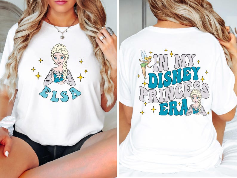 May include: A white t-shirt featuring a graphic of Elsa on the front with the name Elsa below. The back of the shirt displays Tinker Bell and Elsa with the text In My Disney Princess Era, surrounded by small yellow star icons throughout the design.