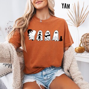 Pu&ograve; includere: Una t-shirt a maniche corte color arancione bruciato con una stampa grafica di quattro fantasmi bianchi e diversi gatti neri. Il testo YAM &egrave; stampato in nero nell'angolo in alto a destra. La maglietta ha un girocollo e una vestibilit&agrave; comoda.