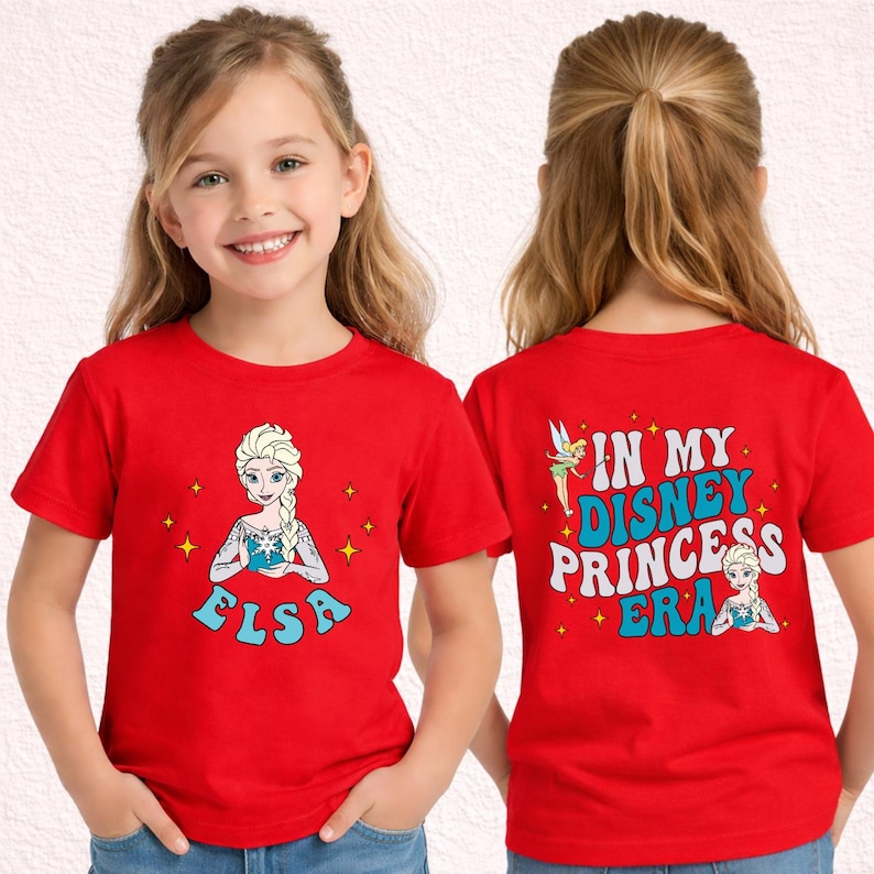 May include: A bright red short-sleeved t-shirt featuring a graphic of Elsa on the front with the name Elsa below. The back displays Tinker Bell and Elsa with the text IN MY DISNEY PRINCESS ERA in blue and white lettering surrounded by yellow stars.