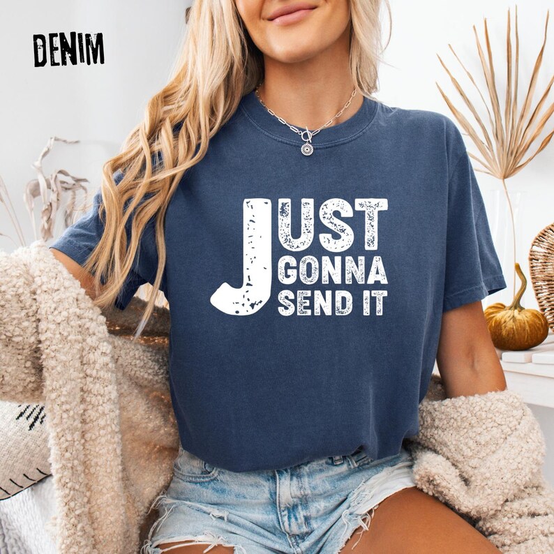 May include: A navy blue t-shirt with the text "JUST GONNA SEND IT" in distressed white lettering. The word "DENIM" is in the upper left corner. The shirt is a casual style.