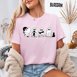 Pu&ograve; includere: Una t-shirt a maniche corte rosa chiaro con una stampa grafica nera di quattro fantasmi che interagiscono con gatti neri. Il testo BLOSSOM &egrave; stampato in nero nell'angolo in alto a destra. Girocollo e vestibilit&agrave; standard.