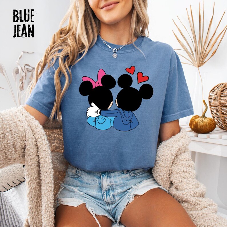 May include: Blue jean short-sleeved t-shirt featuring a graphic of two cartoon mice embracing, with red heart accents. One mouse has a pink bow. The text "BLUE JEAN" is printed in black block letters in the upper left corner.