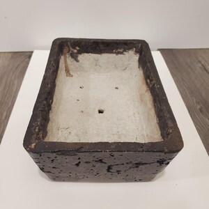 K&ouml;nnte beinhalten: Rechteckiger, dunkelbrauner Pflanztopf mit strukturierter Au&szlig;enseite und hellgrauer Innenseite. Der Pflanztopf hat ein schlichtes Design, geeignet f&uuml;r verschiedene Pflanzen. Die Kanten sind leicht abgenutzt, was ihm ein rustikales Aussehen verleiht.