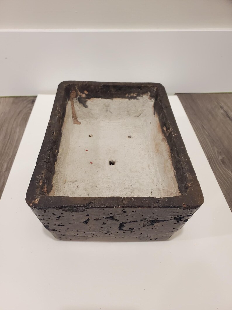 K&ouml;nnte beinhalten: Rechteckiger, dunkelbrauner Pflanztopf mit strukturierter Au&szlig;enseite und hellgrauer Innenseite. Der Pflanztopf hat ein schlichtes Design, geeignet f&uuml;r verschiedene Pflanzen. Die Kanten sind leicht abgenutzt, was ihm ein rustikales Aussehen verleiht.