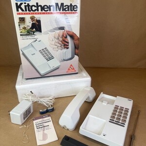 May include: A vintage GTE Kitchen Mate cordless telephone set. The white phone includes a base, handset, charger, and antenna. The box features the product name and a woman using the phone in a kitchen setting.