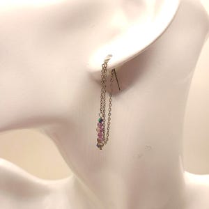 May include: A silver-toned threader earring featuring a delicate chain that loops through the earlobe. The earring is accented with a vertical row of four small, translucent, light purple and iridescent beads at the end of the chain.