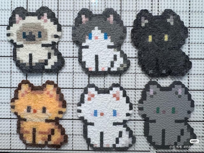 May include: Six pixelated cat-shaped patches in various colors: tan, black, orange, white, and gray. Each cat has a unique color scheme and facial features, with small eyes and a sitting pose. The patches are arranged on a grid.