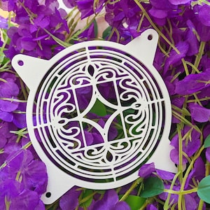 Puede incluir: Una cubierta de ventilador decorativa de metal blanco con un diseño intrincado y arremolinado. La cubierta tiene cuatro pestañas redondeadas con agujeros para el montaje. El fondo es un lecho de vibrantes flores moradas y hojas verdes.