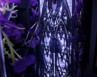 May include: A computer case with a decorative black panel featuring an intricate gothic design. Purple flowers cascade around the case, adding a touch of color. The interior is illuminated with a soft, purple glow.