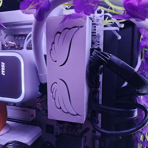 May include: A computer case component with a light purple finish, featuring a carved wing design. The component is surrounded by purple artificial flowers and is part of a computer build. The MSI logo is visible.