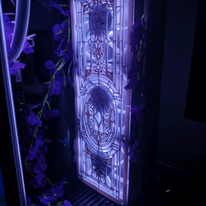 Peut inclure: Un boîtier d'ordinateur avec un panneau décoratif éclairé présentant un motif de vitrail. Le panneau est éclairé d'une douce lumière bleue, et des fleurs violettes sont drapées autour du boîtier, créant une esthétique unique.