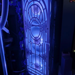 Op de afbeelding: Een computerkast met een wit, sierlijk voorpaneel met een geometrisch ontwerp. De kast heeft blauwe LED-verlichting die het interieur verlicht, wat een coole, futuristische uitstraling creëert. Paarse bloemaccenten voegen een vleugje kleur toe.