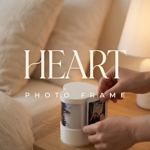 May include: A white heart-shaped photo frame with a rotating design, displaying two small photos. The frame is on a wooden nightstand, with the text "HEART PHOTO FRAME" and "A KEEPSAKE FOR YOUR LOVE STORY".