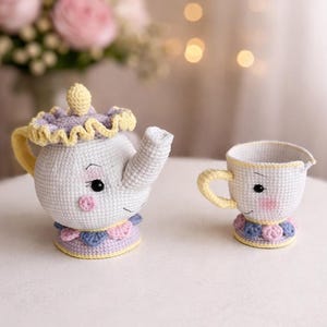 Puede incluir: Juego de tetera y taza de ganchillo en blanco, amarillo, rosa y azul. La tetera tiene tapa y boquilla, con una cara sonriente y adornos decorativos. La taza tiene asa y una cara a juego. El juego es artesanal y caprichoso.