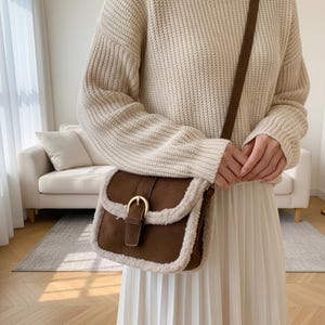 Può includere: Una borsa a tracolla marrone con chiusura a patta e fibbia color oro. La borsa ha un bordo in ecopelliccia e una tracolla marrone. La borsa è realizzata in materiale scamosciato.