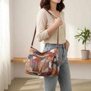 Puede incluir: Bolso de hombro patchwork multicolor con correa y detalles de cuero marrón. El bolso presenta un diseño geométrico con varios colores, incluyendo rojo, azul, naranja y marrón. Tiene un bolsillo con cremallera y un detalle trenzado.