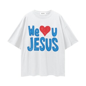 Puede incluir: Camiseta blanca con el texto "We ❤️ U JESUS" en azul y un corazón rojo. La camiseta tiene cuello redondo y mangas cortas. La marca "ROSANNA" está impresa en el cuello.