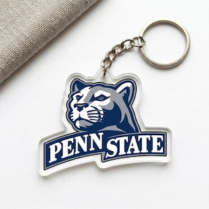 May include: Clear acrylic keychain featuring a cougar head logo in navy blue and gray, with the text "PENN STATE" in white on a navy blue banner. The keychain has a silver chain and ring.