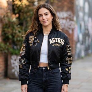 Könnte beinhalten: Schwarze Bomberjacke mit gesticktem Tiger und dem Text "WILDHEART LTD. ED." auf dem Ärmel. Die Jacke hat Aufnäher mit dem Text "ASTRID", "96" und "CUSTOM MADE". Goldene Sterne und andere Details verzieren die Jacke.