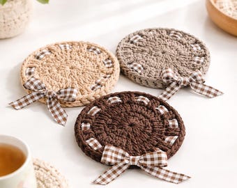 Sottobicchieri neutri all'uncinetto con fiocco a quadretti marroni, decorazioni rustiche per tavolino da caffè nei toni del cioccolato e del beige.