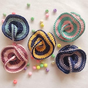 Può includere: Cinque oggetti circolari all'uncinetto con design intrecciati e piegati in varie combinazioni di colori, tra cui blu e verde, rosa e verde, giallo e blu, rosa e viola, e blu e bianco, sparsi con piccole perline colorate.