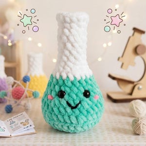 Op de afbeelding: Een gehaakt pluche laboratoriumflesje met een witte hals en een turquoise basis. Het flesje heeft twee zwarte plastic ogen, een geborduurde zwarte glimlach en twee kleine roze geborduurde wangen. De textuur is zacht en grofmazig van structuur.