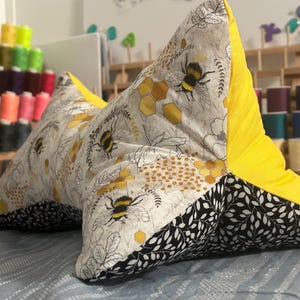 May include: A handmade, star-shaped reading pillow. The pillow features a bee and honeycomb pattern on a gray background, with black and white leaf accents. The back is bright yellow.
