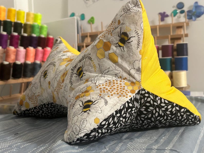May include: A handmade, star-shaped reading pillow. The pillow features a bee and honeycomb pattern on a gray background, with black and white leaf accents. The back is bright yellow.
