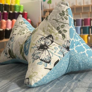 May include: A butterfly-themed reading pillow with a light blue and white floral pattern. The pillow features a butterfly print on a white background, with light blue accents and a quilted design. The pillow is designed for comfort and support.