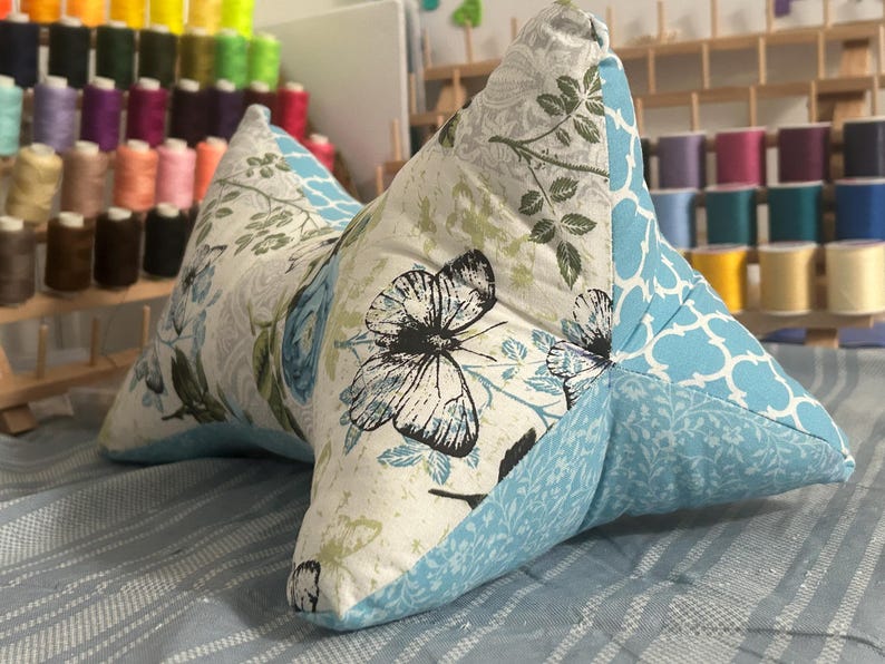 May include: A butterfly-themed reading pillow with a light blue and white floral pattern. The pillow features a butterfly print on a white background, with light blue accents and a quilted design. The pillow is designed for comfort and support.