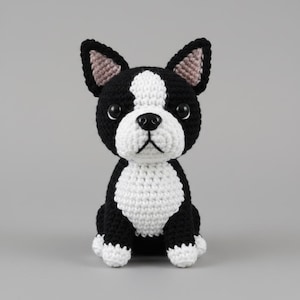 May include: A handmade crochet Boston Terrier dog with black and white yarn. The dog has a white chest, face, and paws, with black ears and body. The dog has a black nose and black eyes. The dog is sitting upright.