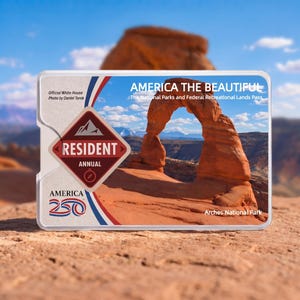 May include: A rectangular America the Beautiful National Parks and Federal Recreational Lands Pass card featuring a photograph of the Delicate Arch in Arches National Park, with text reading Resident Annual, America 250, and Official White House Photo.