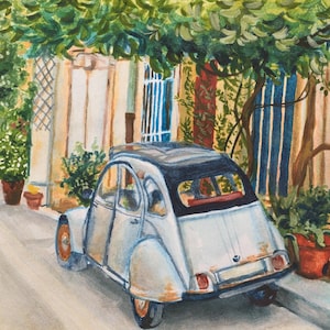 May include: Watercolor painting of a light blue vintage car parked on a cobblestone street. The car has a black roof and orange wheels. The scene is set in a European town with lush greenery and colorful buildings.