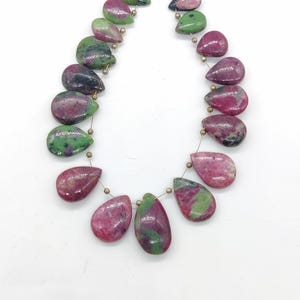May include: A necklace of teardrop-shaped beads. The beads are a mix of pink, green, and black, strung together with gold-colored wire. The beads are smooth and polished, with a natural, organic look.