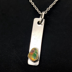 Op de afbeelding: Zilveren hangerketting met een rechthoekige hanger met een kleurrijke, iriserende edelsteen. De edelsteen is gezet in een zilveren bezel. De ketting heeft een fijne zilveren ketting.