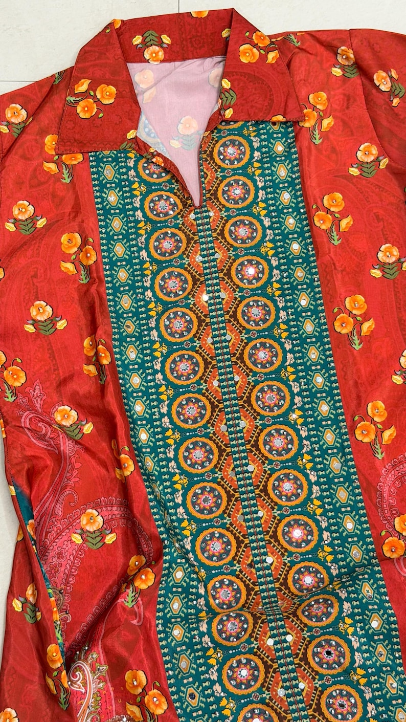 May include: A red collared shirt with a floral and geometric pattern. The shirt features a central panel of teal and gold geometric designs, bordered by red fabric with yellow floral accents. The collar and sleeves also have floral patterns.