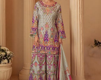 May include: A light gray embroidered salwar kameez set. The long-sleeved top and wide-legged pants feature intricate patterns in purple, pink, and gold. A matching scarf with similar detailing drapes to the side. The outfit is embellished with small beads.