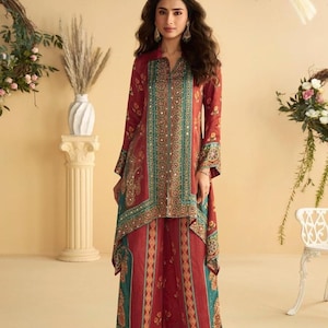May include: A burgundy two-piece outfit, comprising a long-sleeved tunic and wide-leg trousers. The ensemble features teal and gold detailing. The tunic has a V-neck and decorative panels. The trousers have a matching pattern, creating a cohesive look.
