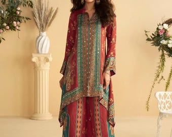 Op de afbeelding: Een tweedelige outfit in bordeauxrood, bestaande uit een tuniek met lange mouwen en een broek met wijde pijpen. De outfit heeft teal en gouden accenten. De tuniek heeft een V-hals en decoratieve panelen. De broek heeft een bijpassend patroon.