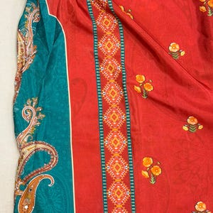 May include: A vibrant textile featuring a bold color palette. The design showcases a rich red background adorned with small floral motifs. A teal panel with paisley patterns and decorative borders adds contrast. The fabric appears to be lightweight and flowing.