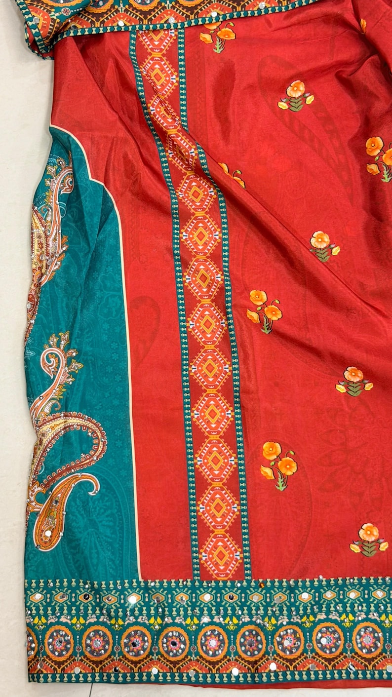 May include: A vibrant textile featuring a bold color palette. The design showcases a rich red background adorned with small floral motifs. A teal panel with paisley patterns and decorative borders adds contrast. The fabric appears to be lightweight and flowing.