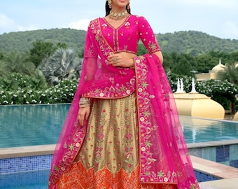 Op de afbeelding: Een levendige roze en gouden Indiase lehenga. De top is een roze blouse met korte mouwen en ingewikkelde borduursels. De rok is goudkleurig met oranje en roze accenten, eveneens geborduurd. Een bijpassende roze dupatta maakt de outfit compleet.
